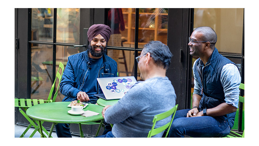 A group of three office workers sit around a table collaborating cheerfully.