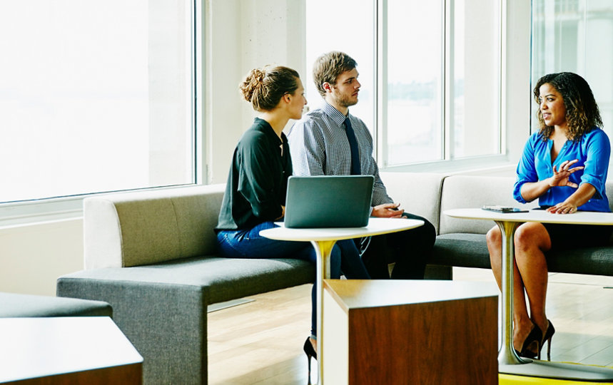 A businesswoman leads a meeting with two colleagues in a sunny office.