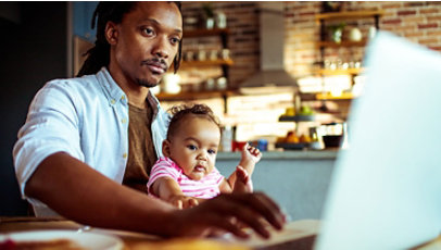 A father holding his infant daughter while working on his laptop