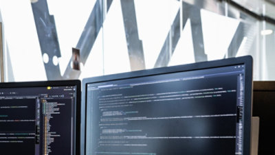 Jumătatea de sus a două monitoare desktop care afișează cod.