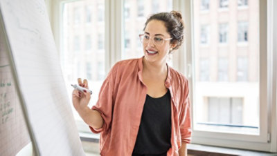 Uma empresária escreve em um flipchart enquanto faz uma apresentação em um escritório.