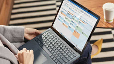Mâinile unei persoane lucrând pe un laptop care afișează un calendar în Outlook.