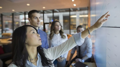 Businesspeople in a meeting room pointing at a projection screen.