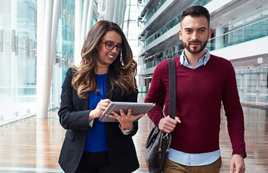 A man and woman walk side by side inside of an office building.