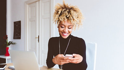 一位女士正在家庭办公室中坐在桌前使用智能手机。