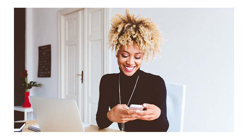 Woman sitting at a desk in a home office using a smart phone.