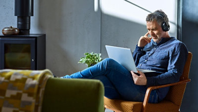 一位男士戴着耳机在听笔记本电脑上的音乐。