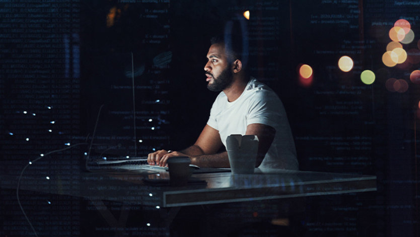 밤에 사무실에서 컴퓨터로 작업하고 있는 프로그래머.