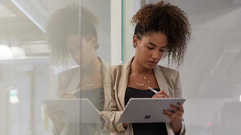산업 사무실에서 태블릿과 스타일러스를 들고 유리벽에 기대어 있는 여성.