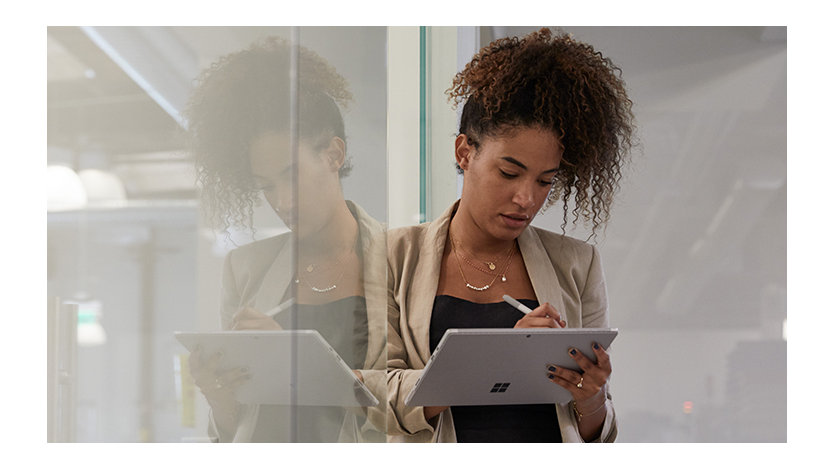 Woman in an industrial office setting leaning against a glass wall while holding a tablet and stylus.