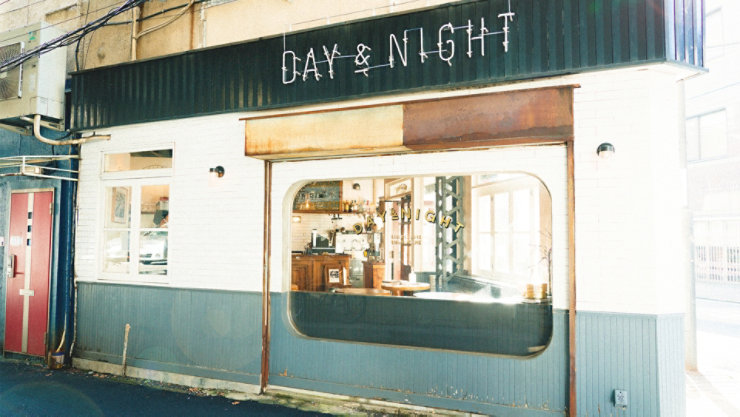 ドアの上に「DAY & NIGHT」と書かれた看板のある建物。これはおそらく都市の路上で、建物の窓が見える屋外のシーンです。