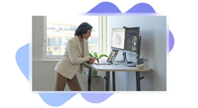A person standing at a desk wearing over-the-ear headphones and using a laptop connected to two desktop monitors.