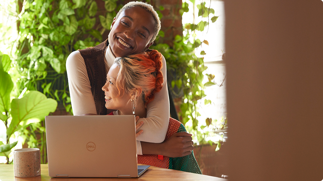 Two women embracing in front of a laptop on a table with illustrated Christmas decorations