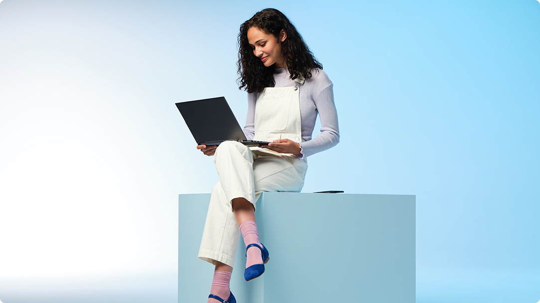 Woman wearing overalls, looking at her laptop with illustrated Christmas decorations