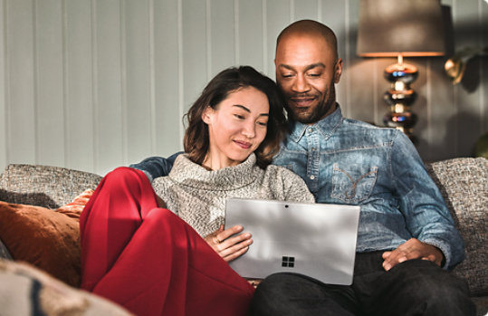 Man and woman sitting on a couch looking at their laptop