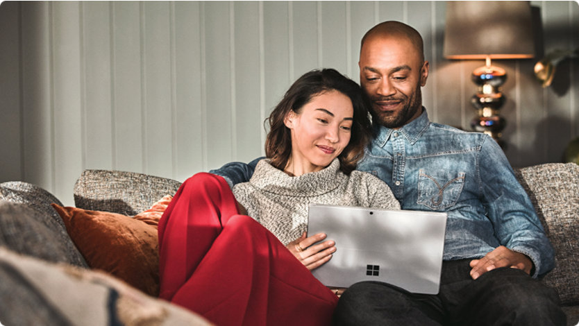 Man and woman sitting on a couch looking at their laptop
