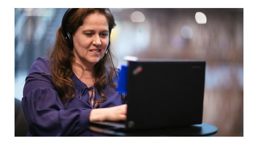 Debra Droz, a woman who is hard of hearing, wears headphones and types on a laptop.