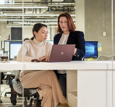 Dve osobe sede za stolom u kancelariji i zajedno gledaju u laptop