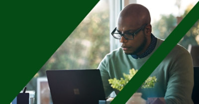 Ein Mann, der vor einem Laptop arbeitet, während er auf einem Schreibtisch sitzt. 