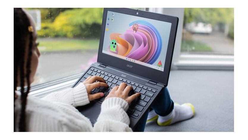 Female student sitting near windows at home and typing on a laptop in her lap.