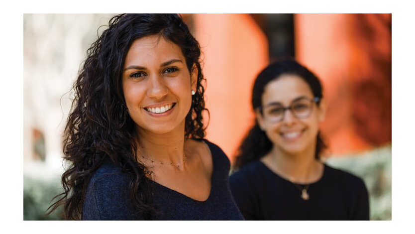 Two female employees face the camera smiling. 