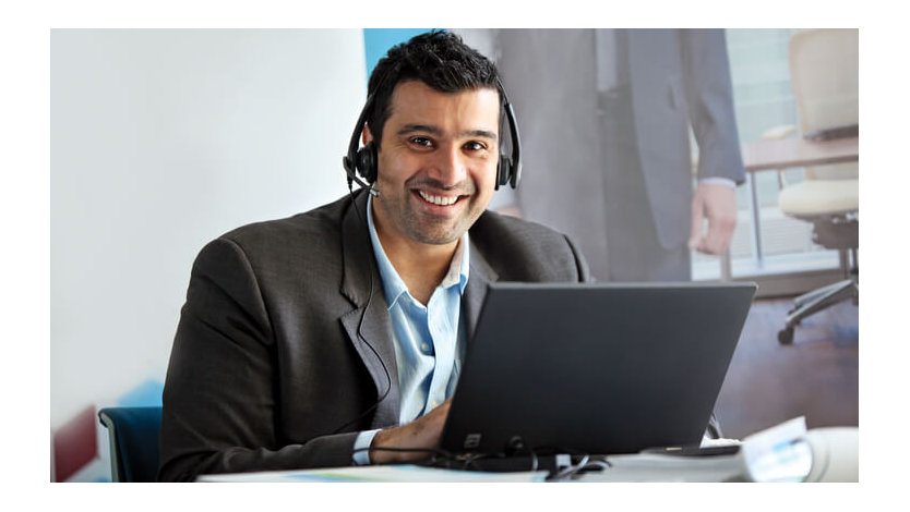 A Microsoft employee smiles as he attends a meeting virtually on his PC with his headset on.