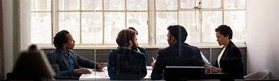 Five people wearing business attire, sitting around a conference table and having a meeting