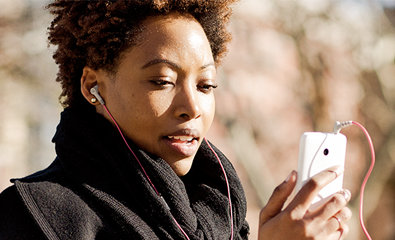 Una persona all'aperto, vestita con abiti caldi, sciarpa e cappotto neri, guarda lo smartphone. Sono visibili alberi e uno sfondo sfocato.
