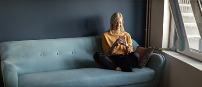 Un uomo con maglia celeste seduto sulle scale esterne, guarda il telefono e sorride.