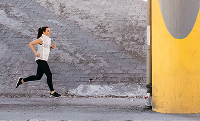 Osoba u sportskoj odeći trči napolju pored velike žute građevine i kamenog zida.