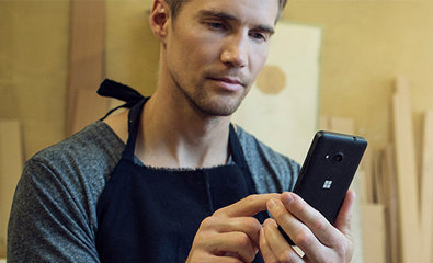 Un uomo con maglia blu guarda lo smartphone con espressione pensierosa mentre tiene in mano uno strumento sulla spalla.