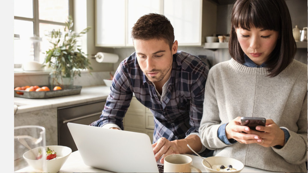 Ein Mann arbeitet am Laptop während eine Frau ihr Handy bedient