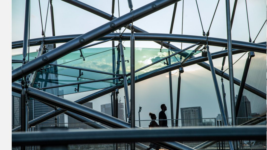 Zwei Personen gehen über eine Brücke. Im Hintergrund sindHochhäuser zu erkennen.