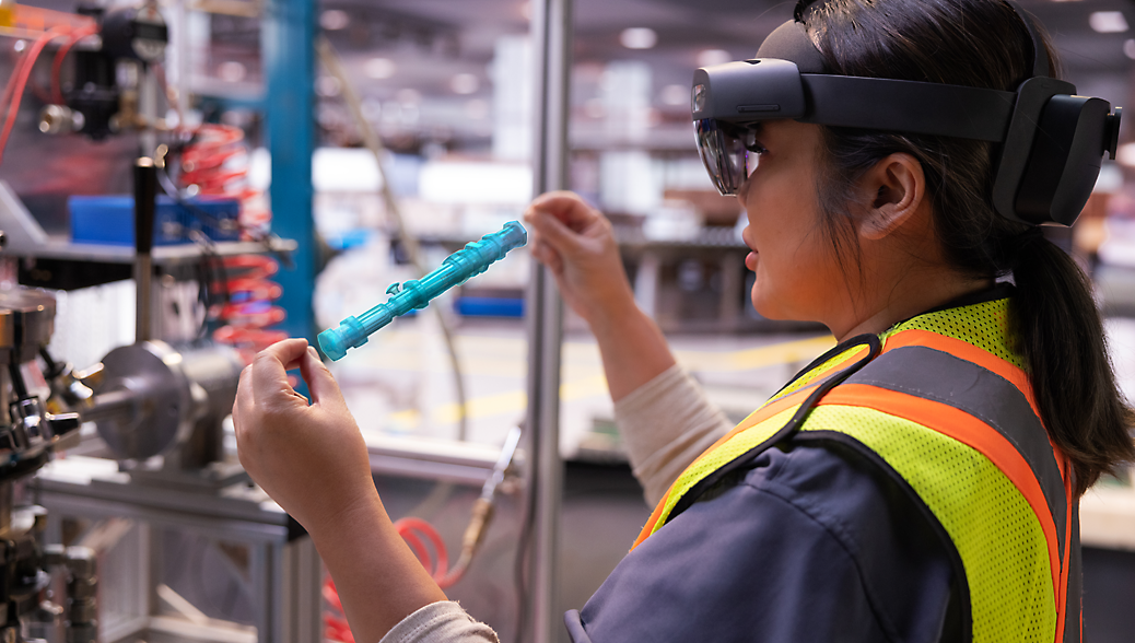 Una ingeniera con un casco VR y un chaleco de seguridad examina una parte mecánica en un entorno industrial.