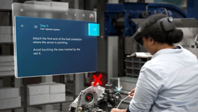 A technician in a factory follows instructions on a digital display while assembling a fuel injection system marked with a red "x.