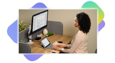 A person sitting at a desk wearing a headset and working on a tablet connected to a desktop monitor.