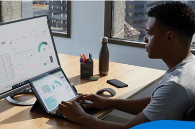 A person sitting at a desk using a laptop connected to a desktop monitor