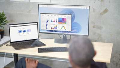 Eine Person, die an einem Schreibtisch sitzt und Daten auf einem Laptop und einem Desktopmonitor anschaut