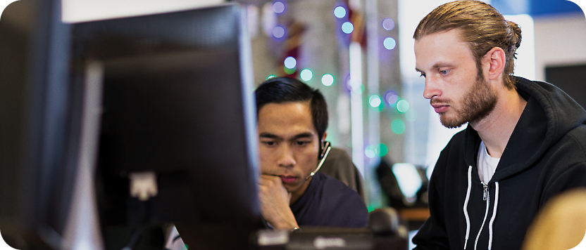Dos hombres centrados en una pantalla de ordenador en una oficina moderna, uno asiático y otro blanco