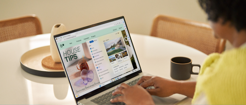 Persona con una camisa amarilla usando un portátil que muestra un sitio web titulado "sugerencias para el hogar" en una mesa de cocina