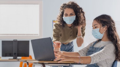 An educator and a student wearing masks looking at a laptop.