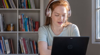 A person wearing over the ear headphones and using a laptop.