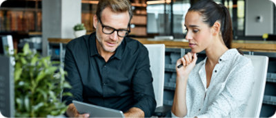 Két személy irodai környezetben ül és egy tabletet néz.