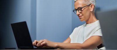 Woman with glasses working on a laptop in an office environment.