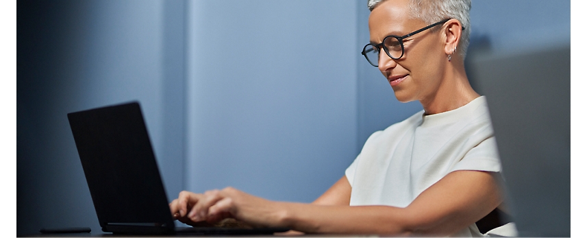 Eine Frau mit Brille arbeitet in einer Büroumgebung an einem Laptop.