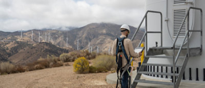 Un hombre con un casco de pie junto a una turbina de viento.