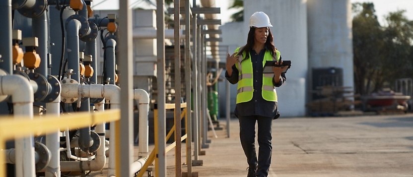 A woman in a hard hat is holding a tablet in her hand