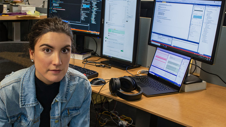 Woman looking at the camera with destop screens behind her