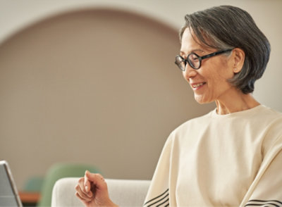 Una mujer con gafas sonriendo y trabajando en su computadora portátil.