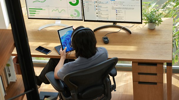 Uma pessoa trabalhando em uma mesa com um tablet e vários monitores de desktop 